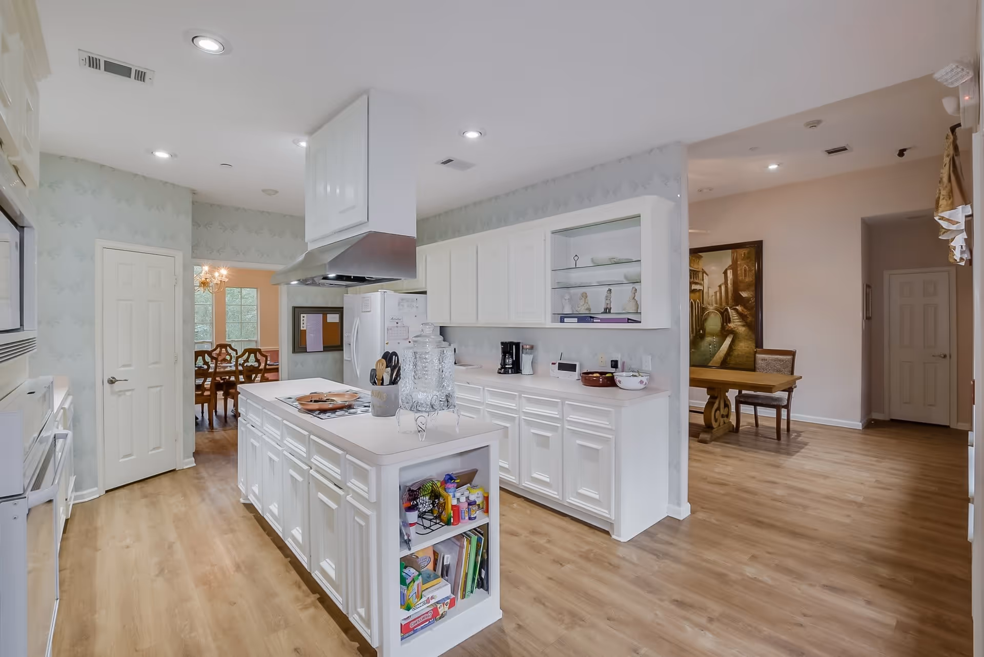 Open white kitchen with a central island, built-in cabinets, and views into a dining area.