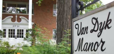 Exterior view of a brick building with a white porch and Van Dyke Manor sign.