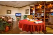 Cozy communal living room with a round table covered in a red cloth set for chess, sofas, bookshelves and a television.