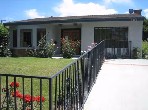 Front view of a single-story senior living facility with a railing and rose bushes.
