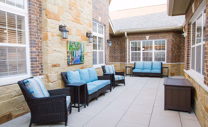 Enclosed sunlit patio with wicker sofas and chairs topped with blue cushions against brick and stone walls.