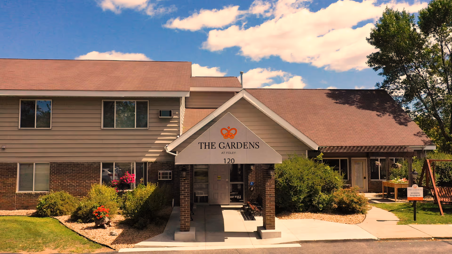 Front entrance of a two-story senior living building with a covered portico reading "The Gardens at Foley" and landscaped grounds.