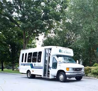 White shuttle bus labeled The Laurels parked on a tree-lined street.