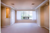 Empty carpeted living room with a large center window, recessed lighting, beige walls, crown molding, and built-in alcoves.