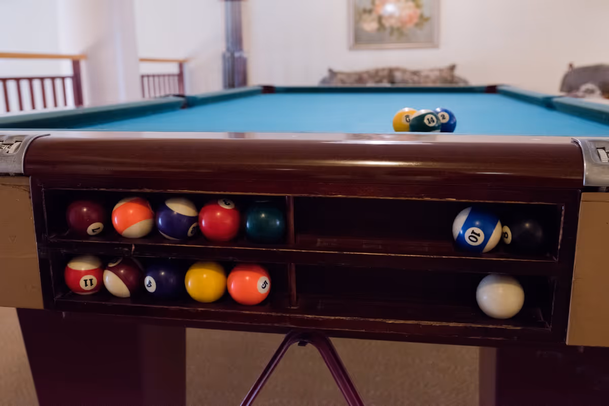 Close-up of a billiards table showing pool balls stored in built-in racks and the teal felt playing surface.