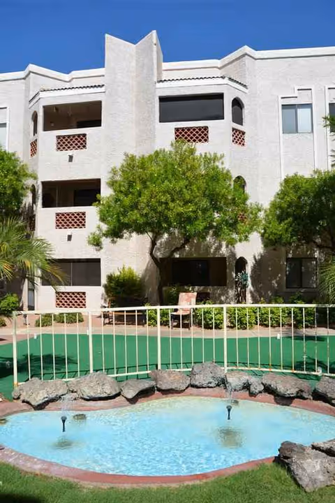 White multi-level senior living building with an outdoor pool and greenery.