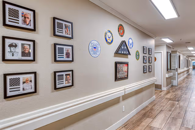 A long interior hallway decorated with framed photos, a folded flag display and military emblems on the wall.