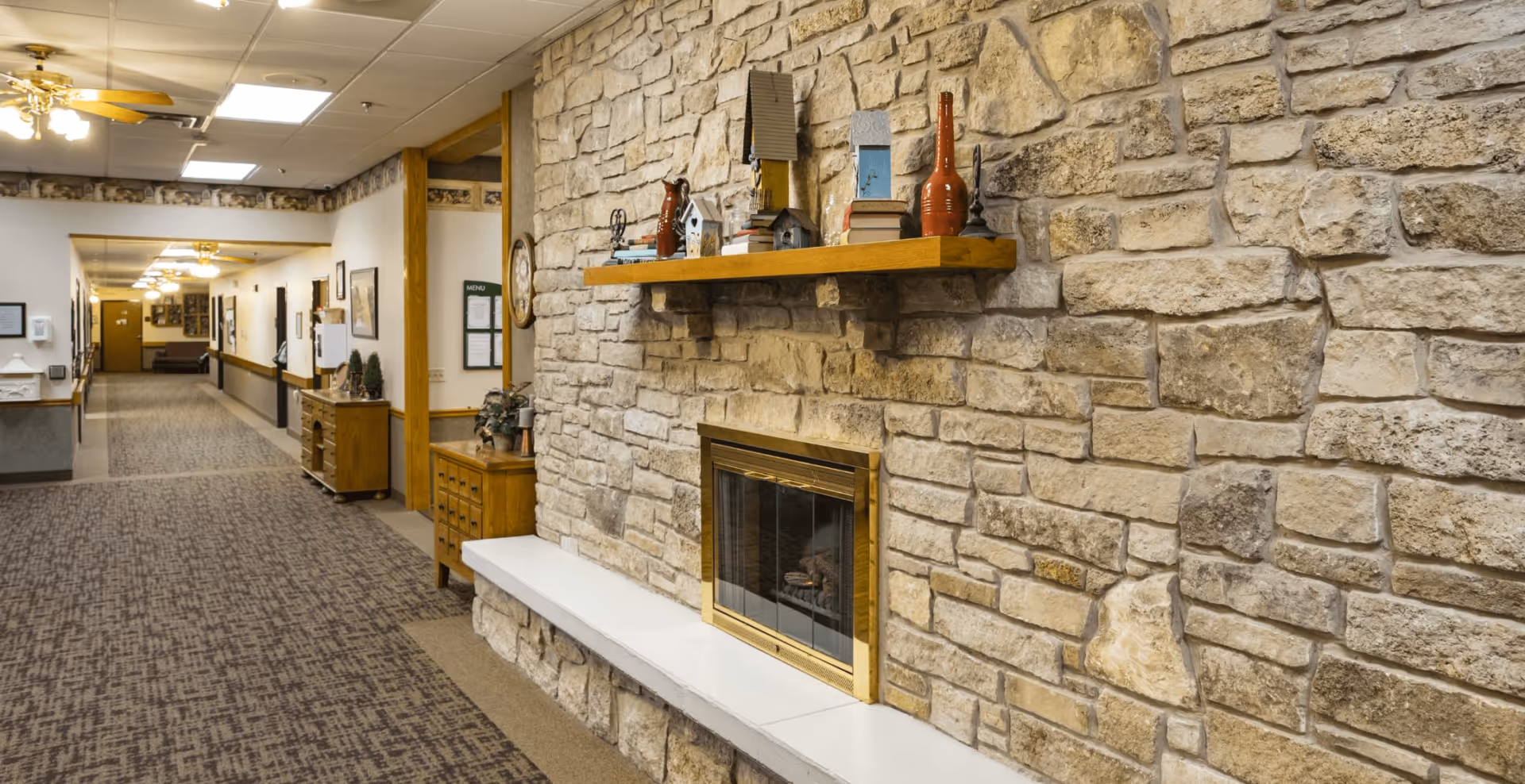 Carpeted interior corridor featuring a stone fireplace wall with a decorative mantel and hallway leading to rooms.