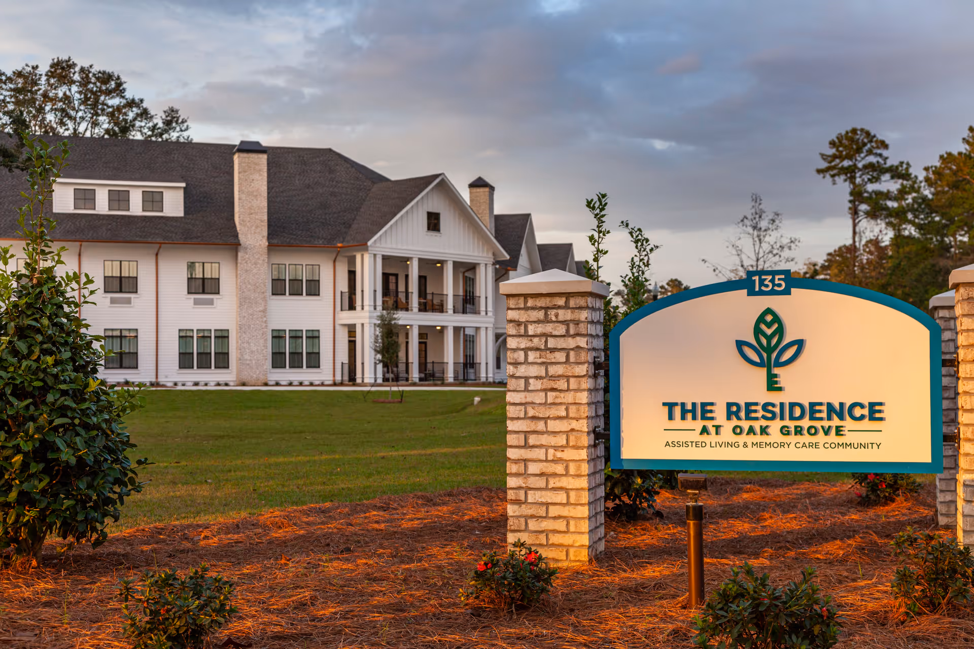 White multi-story assisted living building with a lawn and a prominent sign reading "The Residence at Oak Grove" in front.