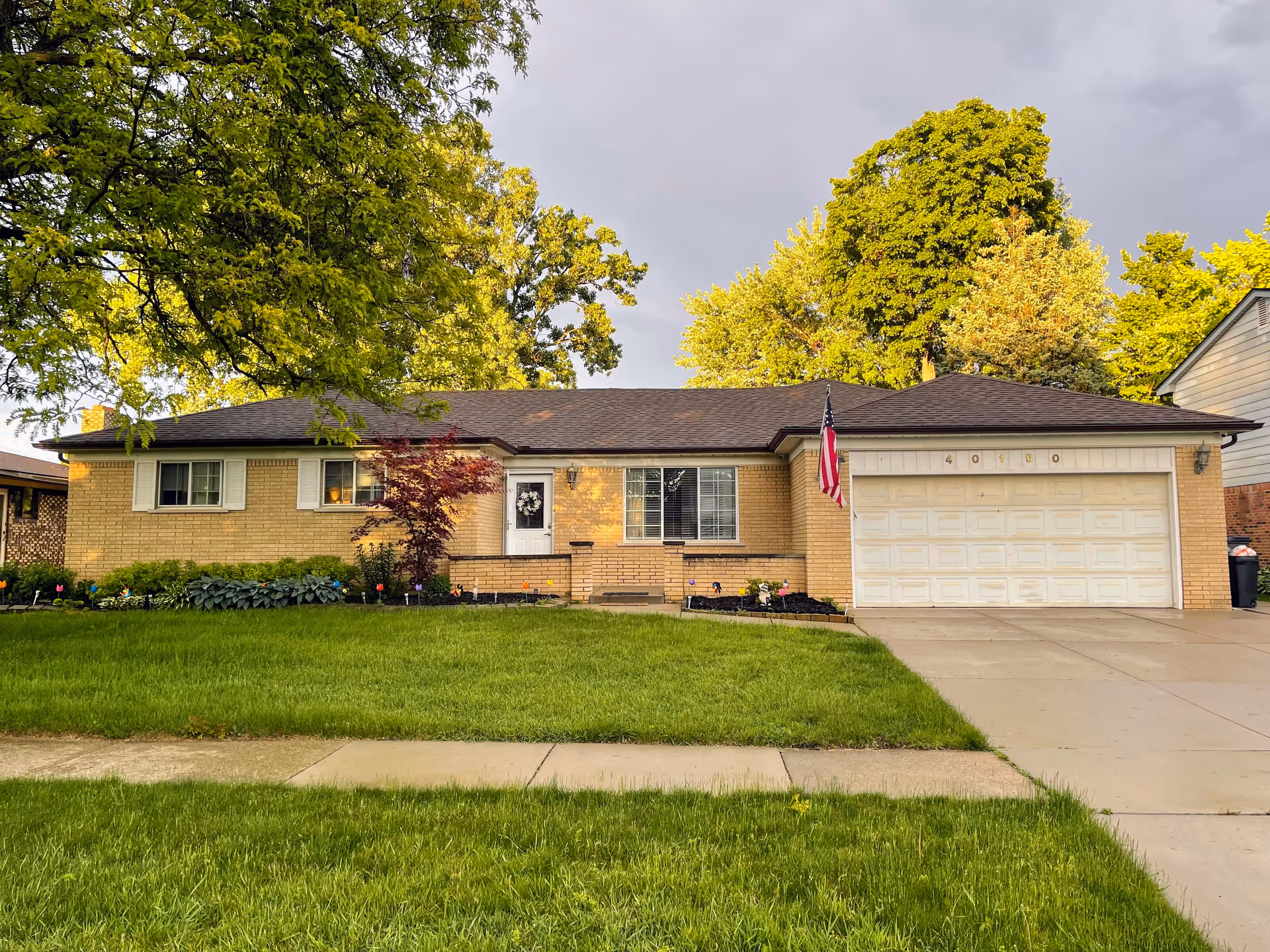 Single-story brick house with a two-car garage, green lawn, and American flag by the entrance.