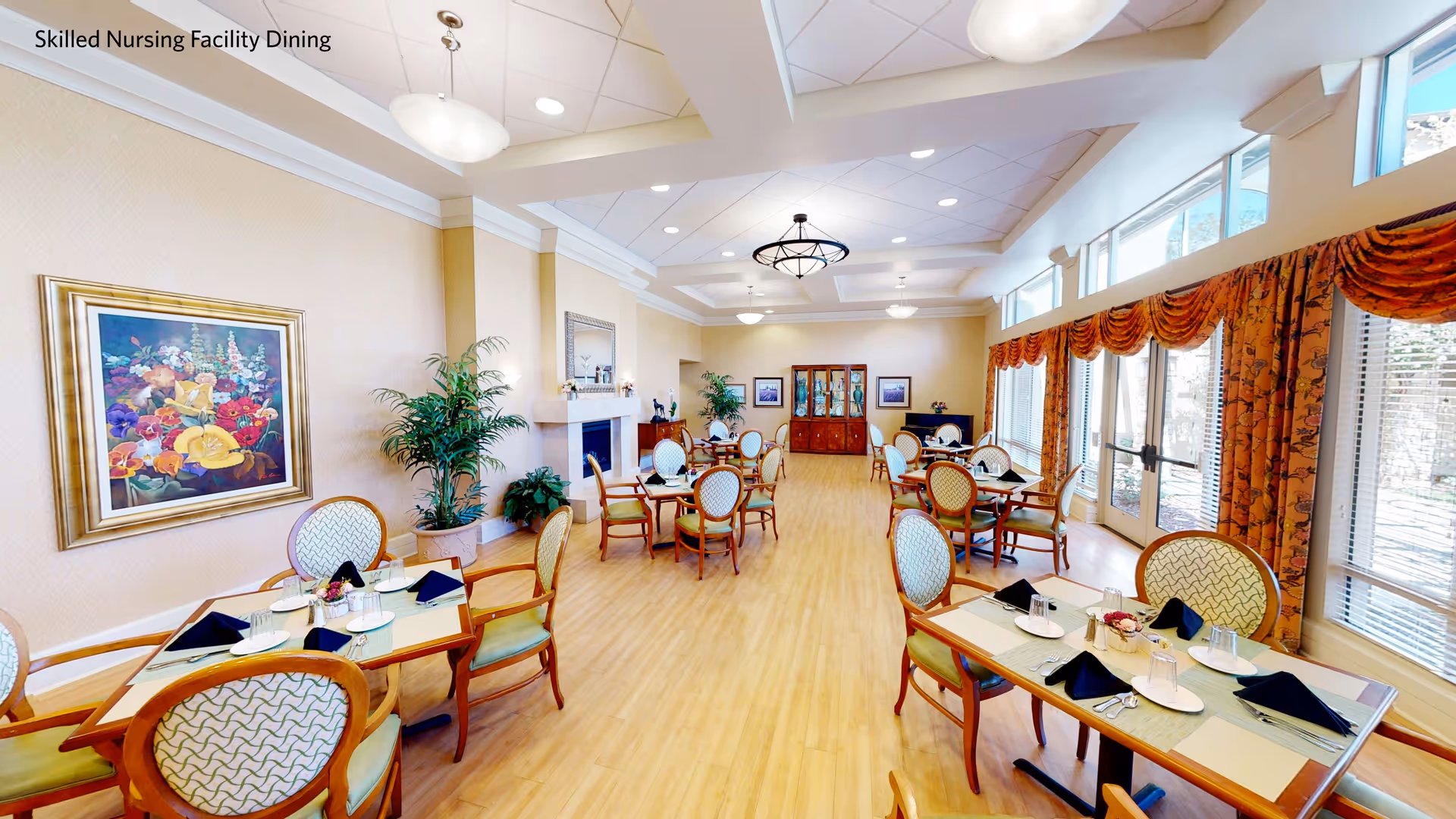 Spacious dining room with multiple set tables and chairs, large windows with drapes, artwork, and plants.