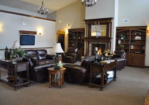 Cozy senior living room with dark leather seating, fireplace, and bookshelves.
