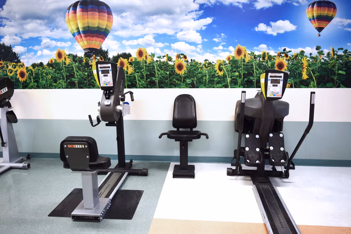 Exercise room with seated workout machines in front of a mural of sunflowers and hot-air balloons.