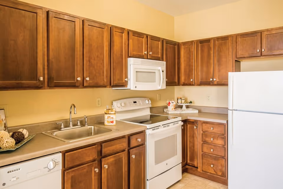 Kitchen with warm wooden cabinets, a sink, white stove and microwave, and a white refrigerator.