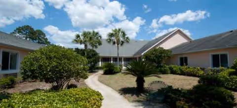 One-story senior living facility exterior with a curved walkway and palm trees.