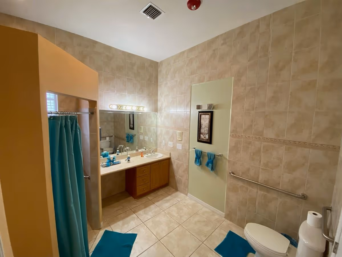 Tile-walled bathroom with a vanity and mirror, sink, toilet, shower with a turquoise curtain, and matching rugs and towels.