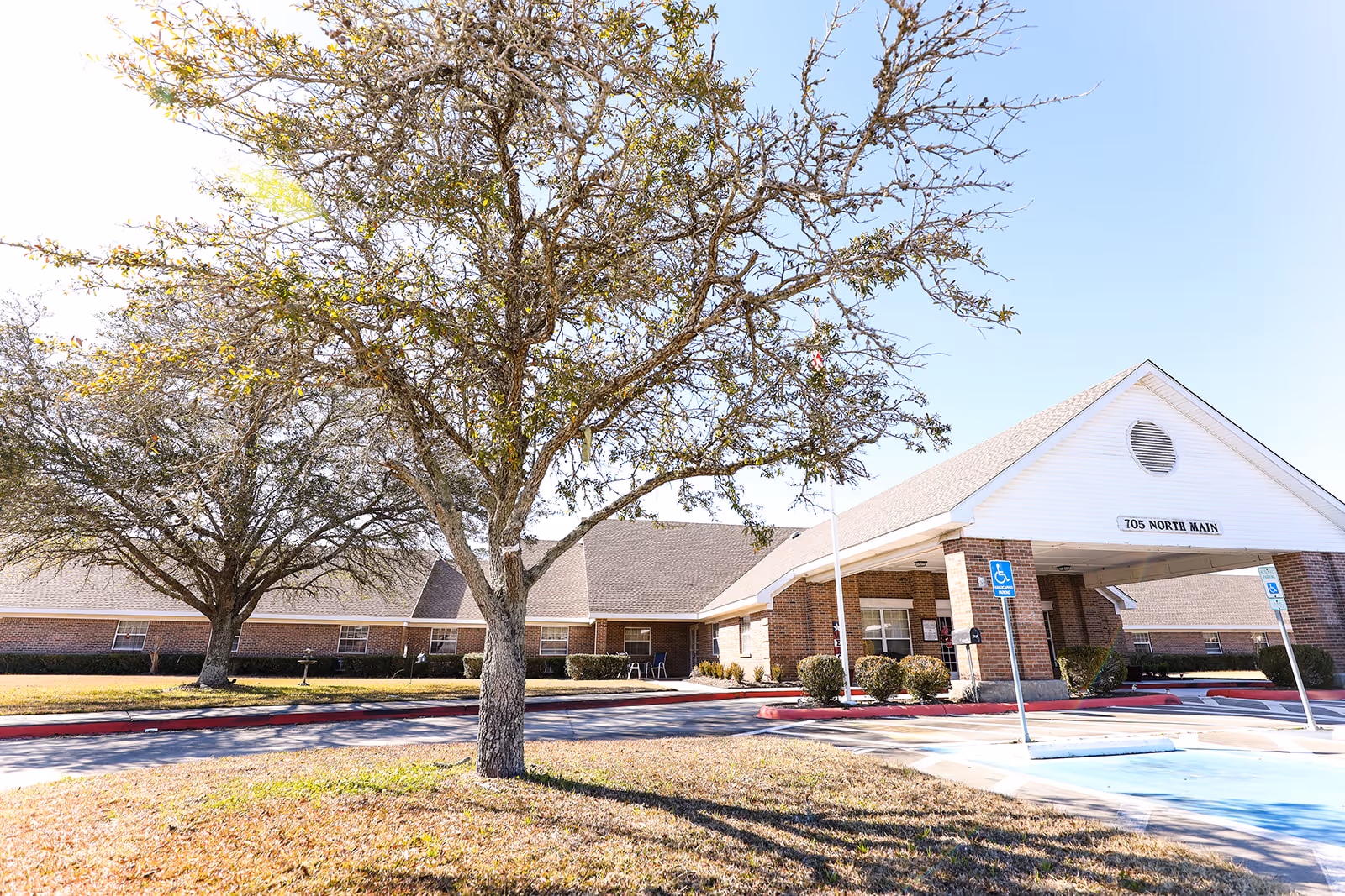 Front exterior of a brick nursing center with a covered entrance, parking spaces, and trees on the lawn.