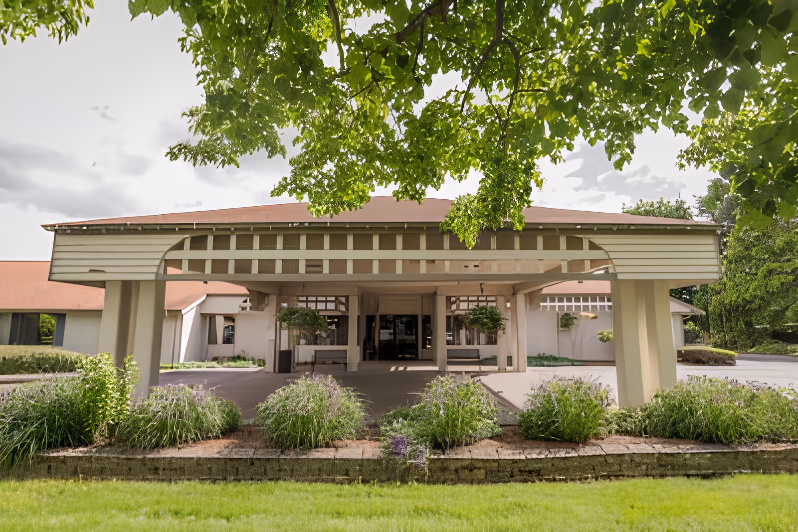 Front entrance with a covered porte-cochère, landscaped planting beds, and overhanging tree branches.