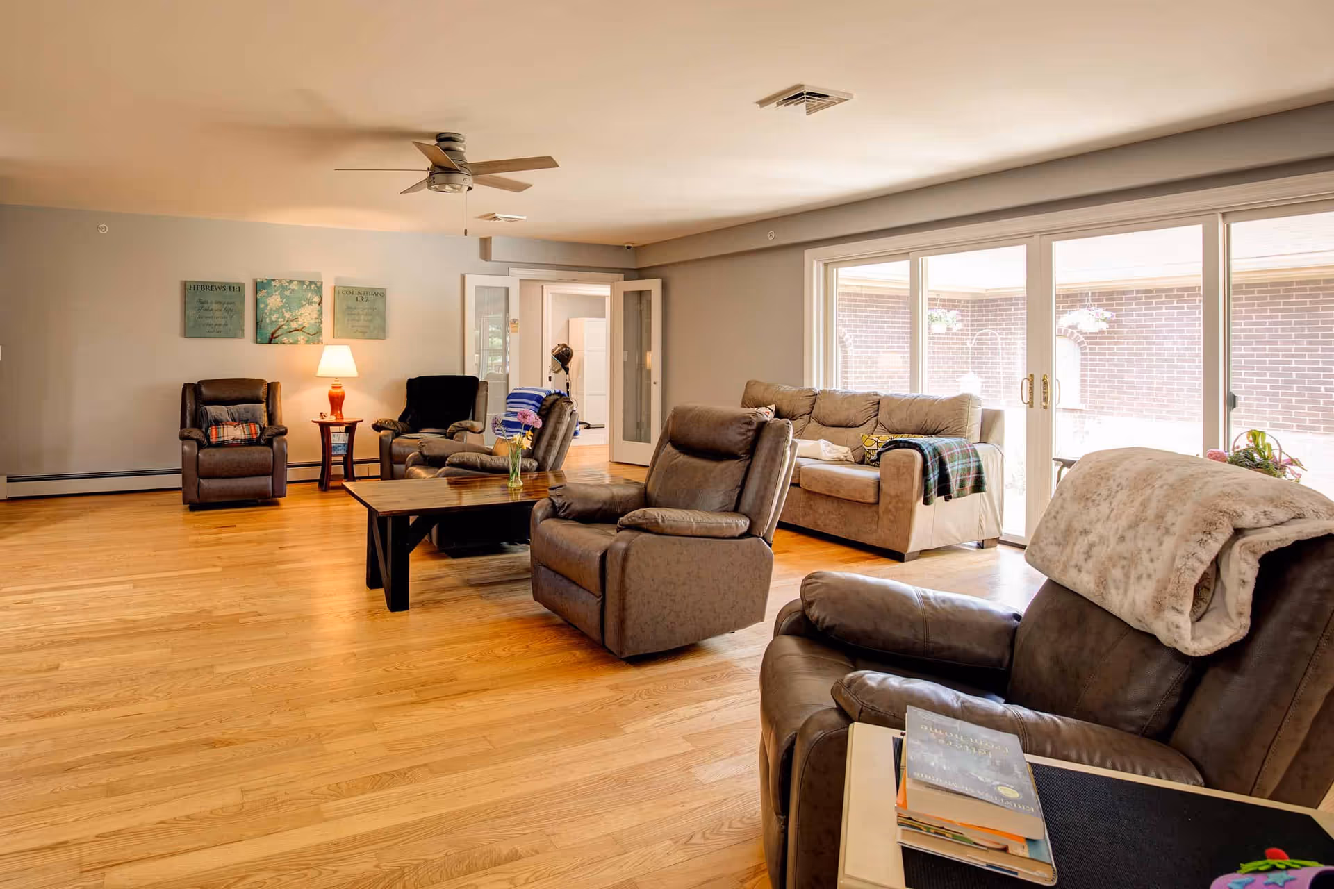 Spacious living room with multiple recliner chairs, a sofa, a coffee table, and large sliding glass doors letting in natural light.