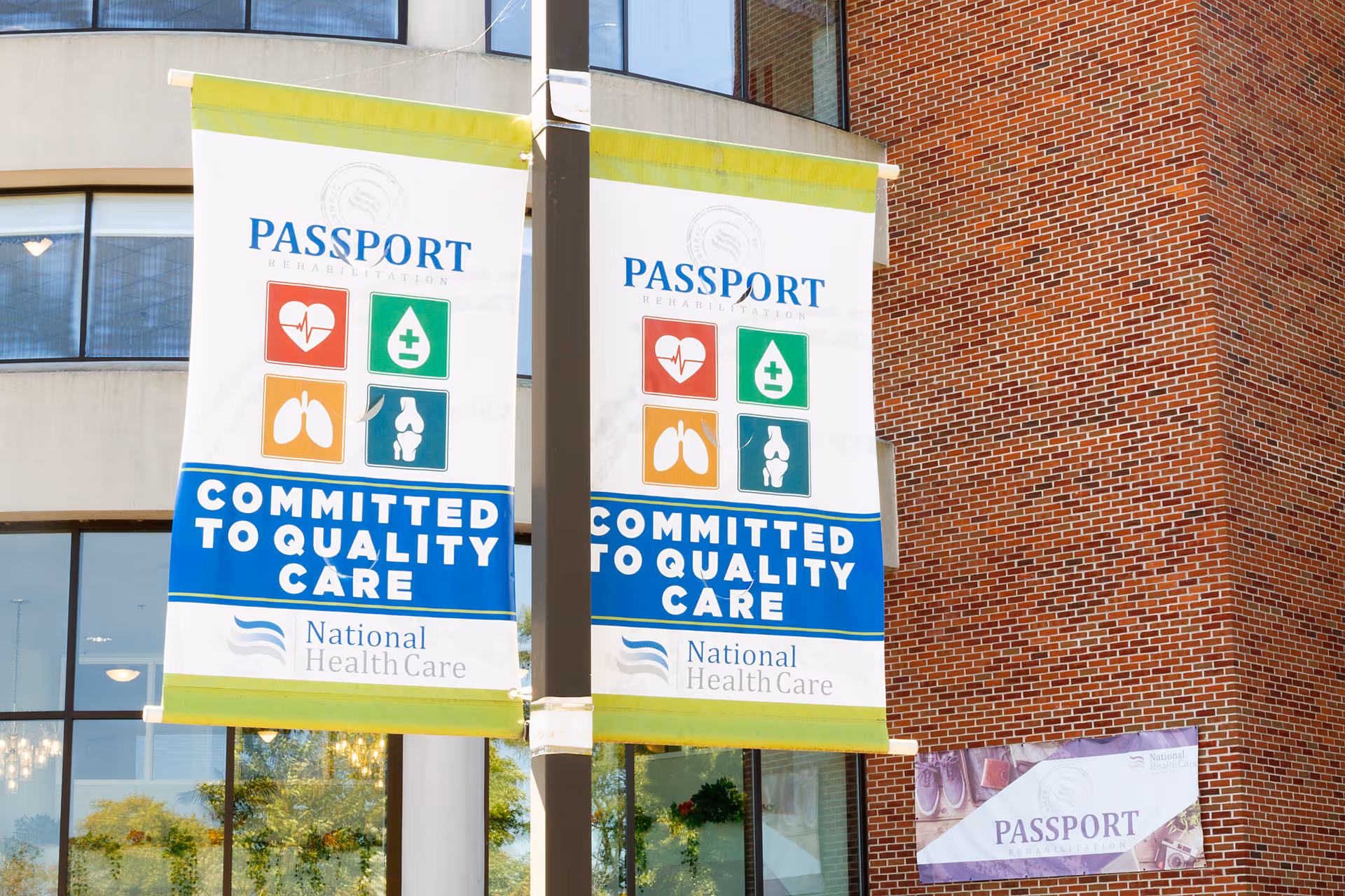 Two vertical 'Passport' health care banners hanging from a pole in front of a brick and glass building.