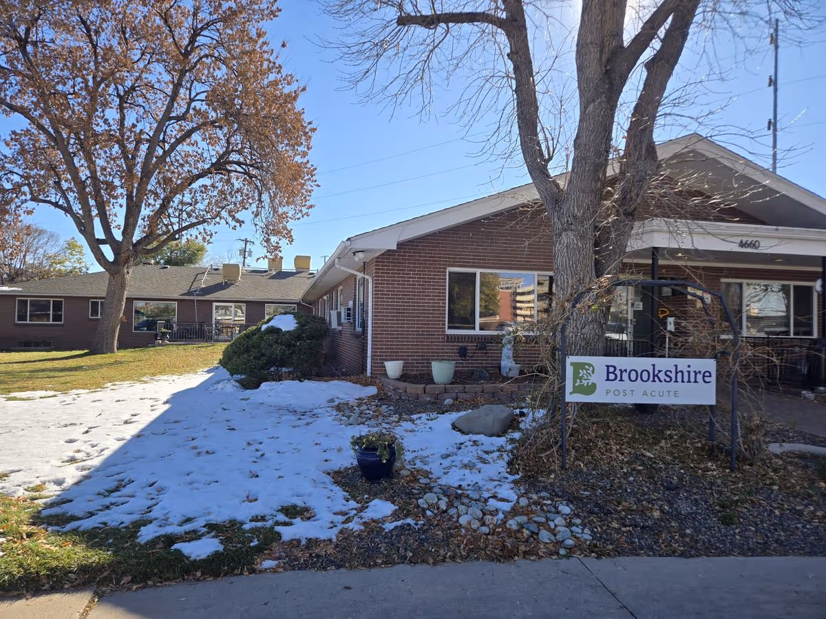 Front exterior of the Brookshire Post Acute brick building with a large tree, patches of snow on the lawn, and a Brookshire sign by the entrance.