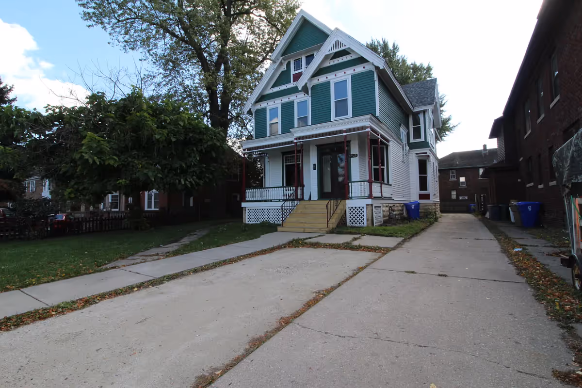 Green-and-white Victorian-style house with a front porch and long driveway leading up to it.