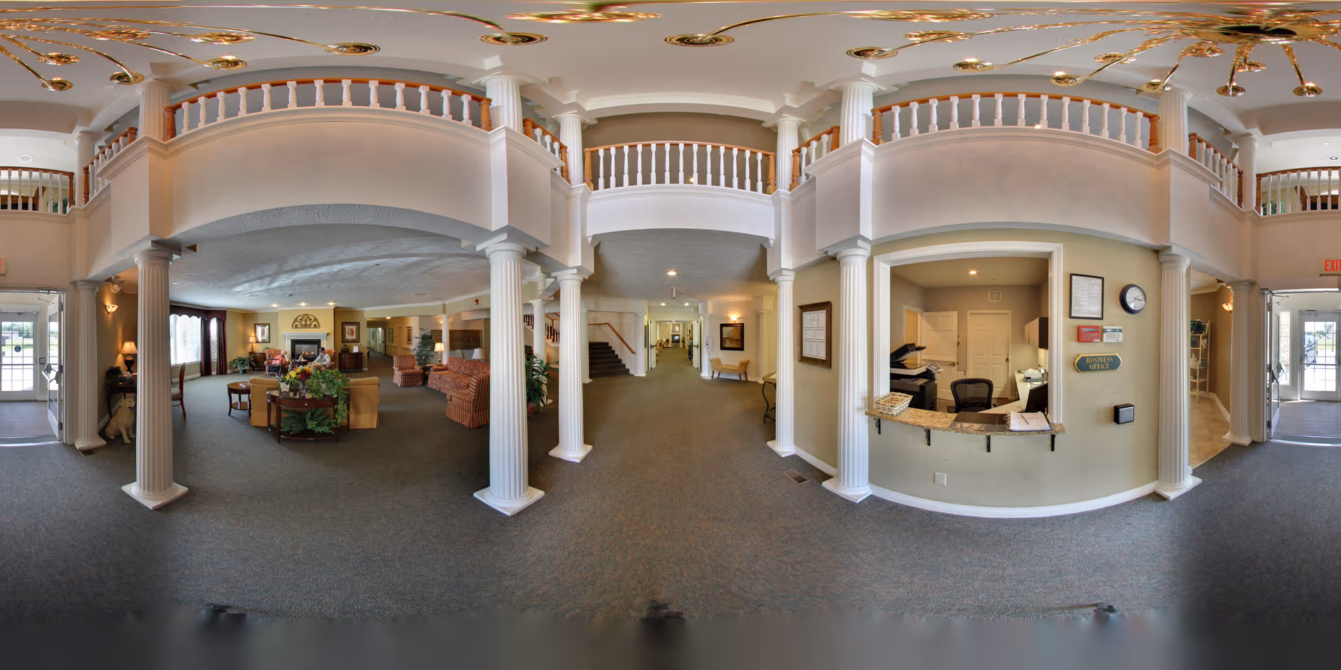 Wide two-story lobby with columns, a reception desk, seating area, and an upstairs balcony.