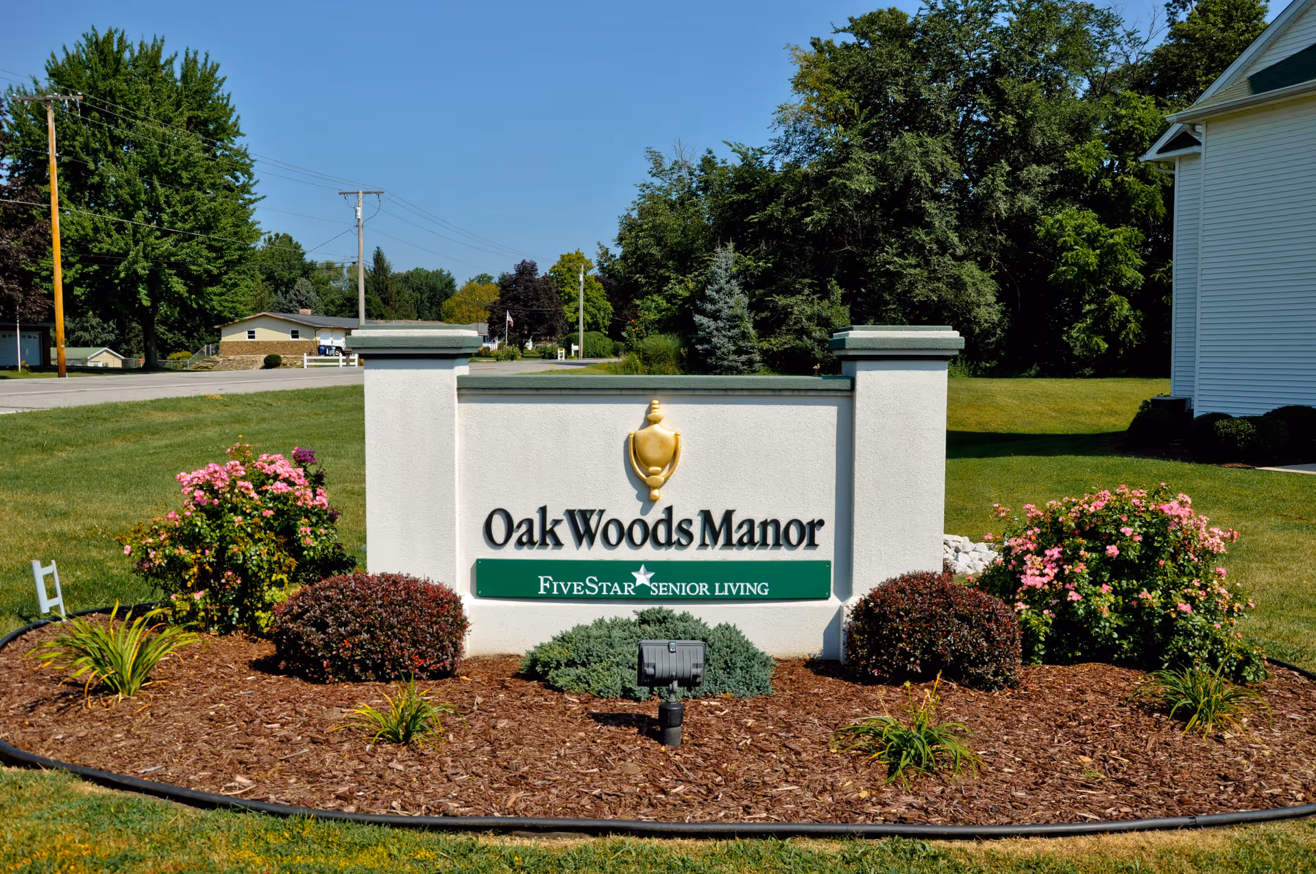 Entrance sign reading 'Oak Woods Manor' with landscaping and lawn in front of a residential building.