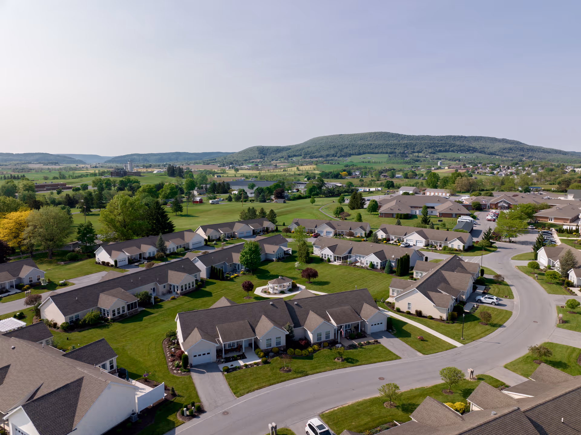 Aerial view of a senior living neighborhood with single-story homes, green lawns, and rolling hills in the distance.