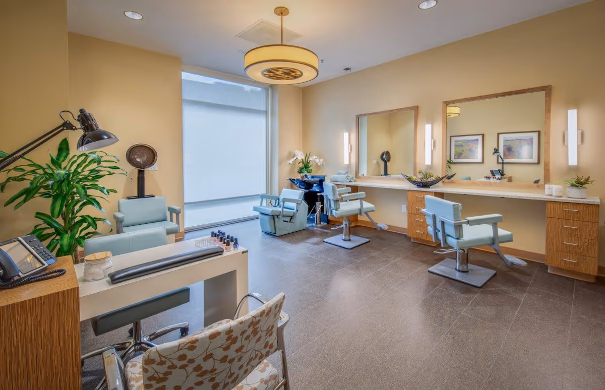 Bright salon room with styling chairs, large mirrors, a manicure station, and decorative plants.