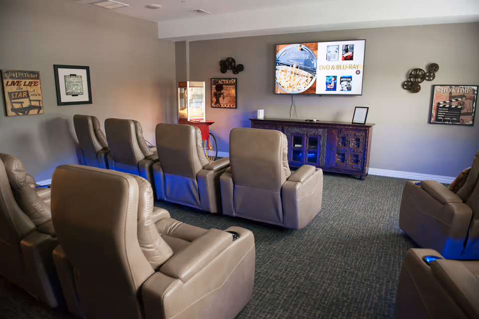 Media room with rows of beige reclining chairs facing a wall-mounted TV and a popcorn machine.