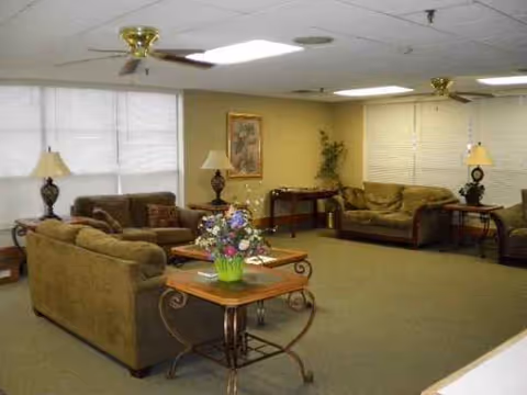 Cozy senior living center lounge with sofas, coffee tables, lamps, and potted plants.