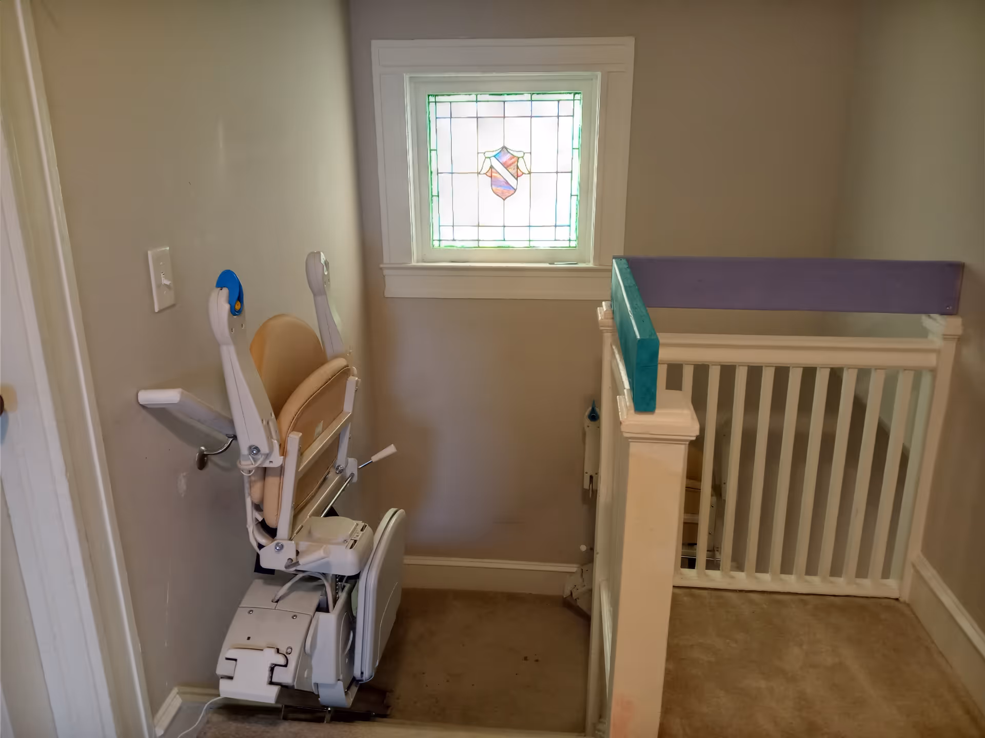 A stairlift chair is installed along a hallway with a window and railing.
