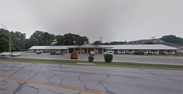 Exterior of Village At Carrol Park senior living facility with parking and trees.