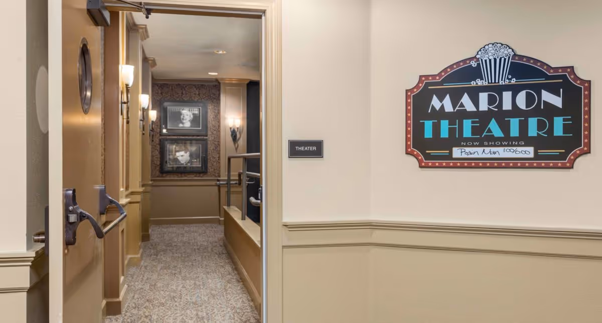 Open double doors leading into a decorated corridor for the Marion Theatre with framed black-and-white photos and a marquee sign on the wall.