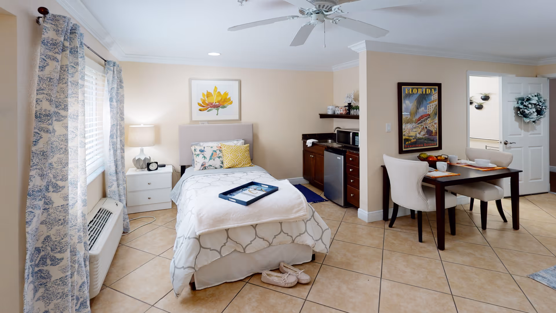 Studio apartment interior with a bed, bedside table, kitchenette and small dining area.