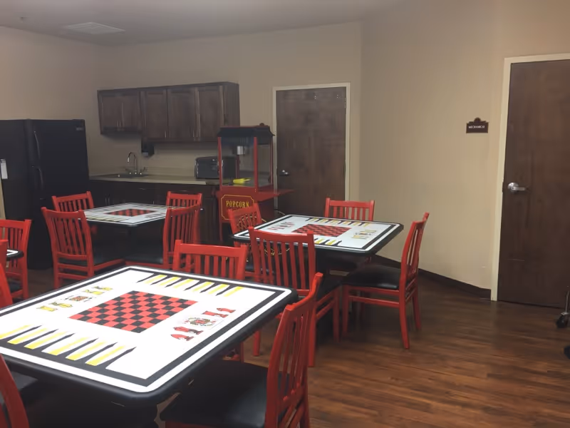 Community dining room with red chairs, game-themed tables, a kitchenette and a popcorn machine.