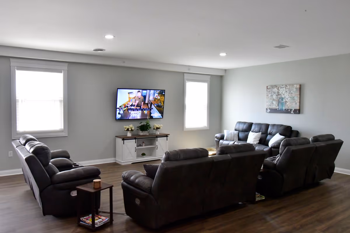 Spacious living room with several dark reclining sofas arranged around a wall-mounted TV and a small console table.