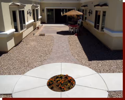 Exterior courtyard of a senior living facility with circular concrete edging, gravel paths, and patio table.