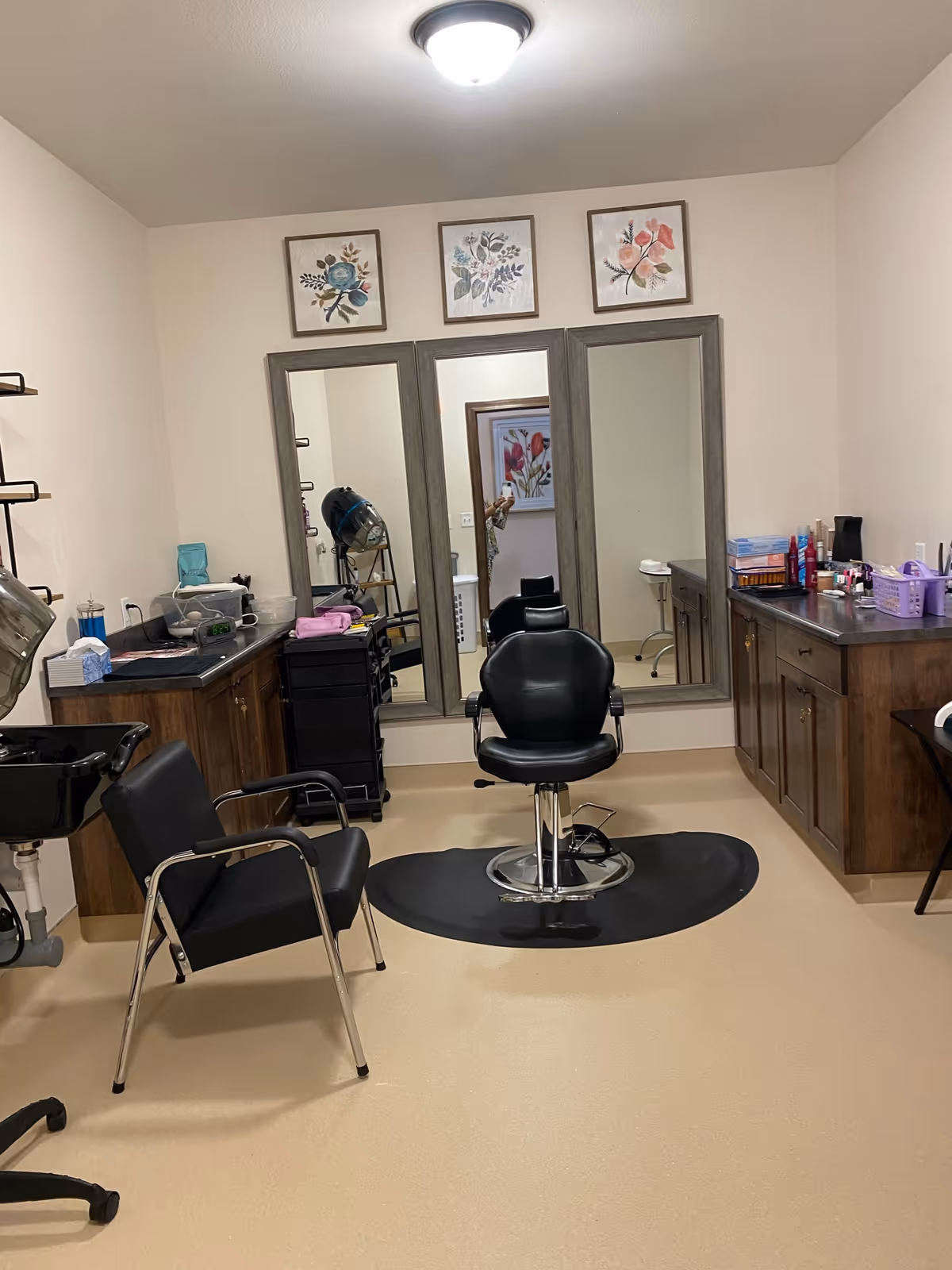 Small salon room with a styling chair in front of three mirrors, cabinets, and hairdressing equipment.