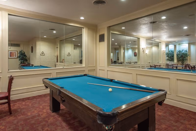 A pool table with a cue and ball sits in a mirrored indoor recreation room.