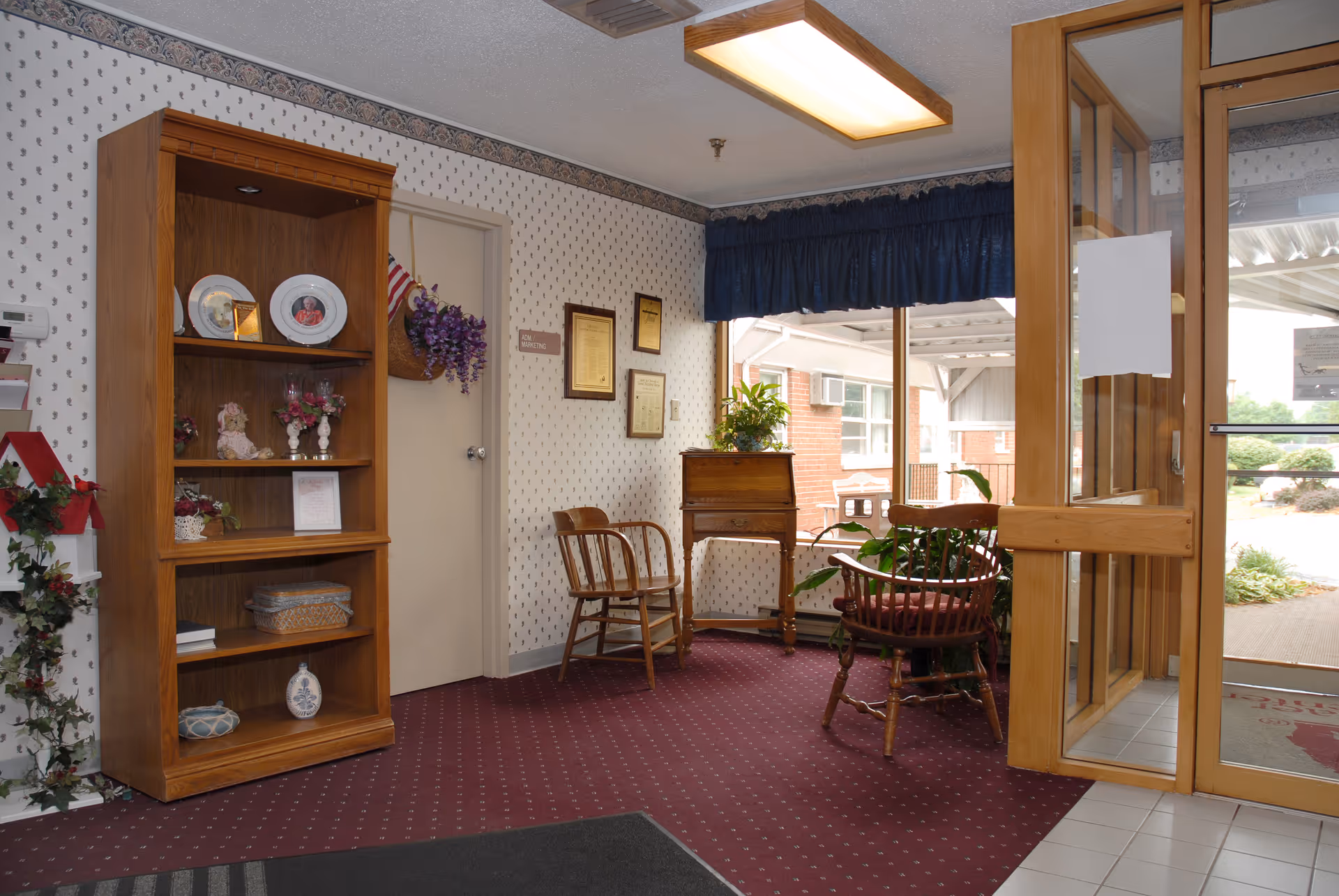 Entrance lobby with wooden shelving, chairs, potted plants, and a glass door leading outside.