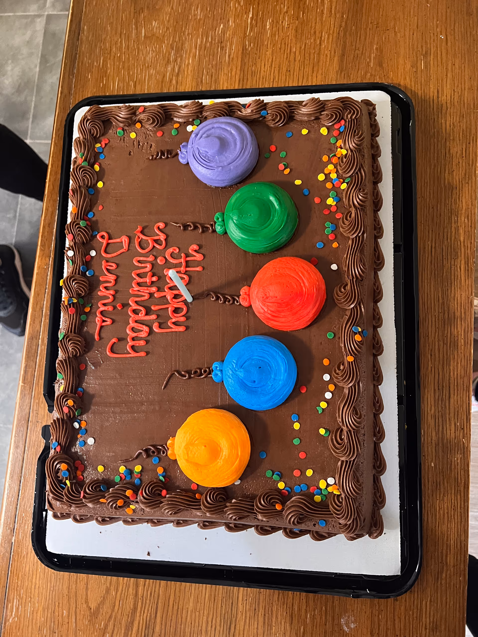 Chocolate sheet birthday cake with colorful balloon frosting decorations and "Happy Birthday Donna" written in red, on a wooden table.