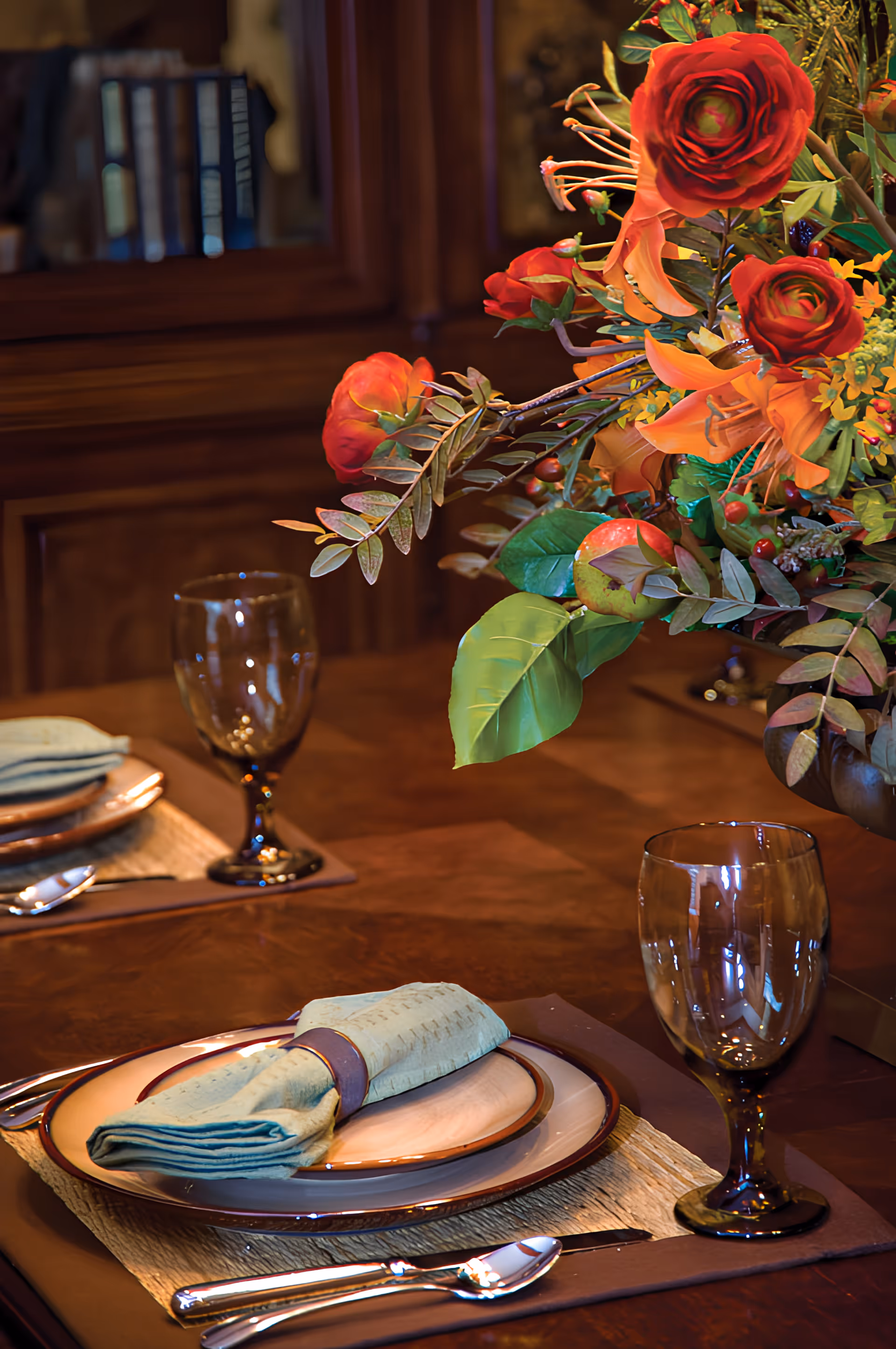Elegantly set dining table with plates, folded napkins, wine glasses and a large floral centerpiece.