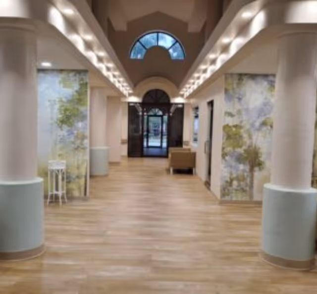 Spacious, well-lit entry hallway with columns, wood flooring, decorative wall panels, seating, and an arched glass doorway at the far end.