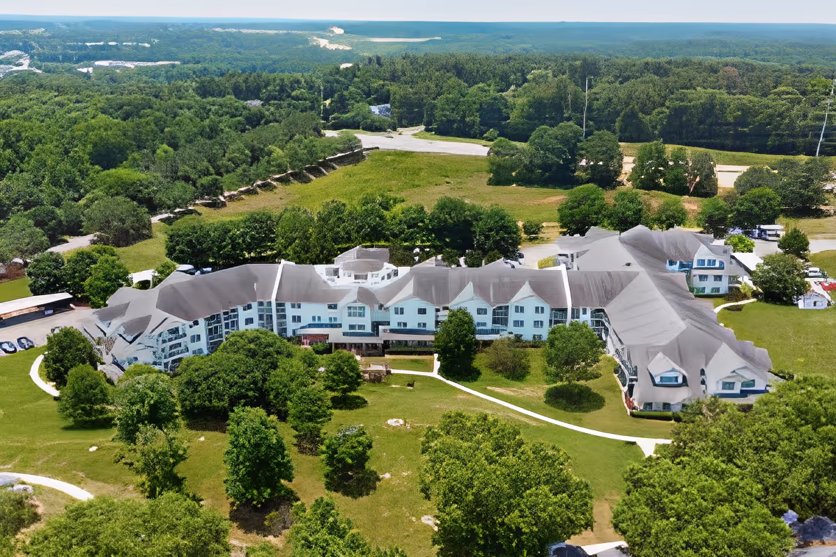 Aerial view of TerraBella Epps Bridge senior living facility surrounded by green trees and grassy areas, with a winding pathway leading to the building entrance.