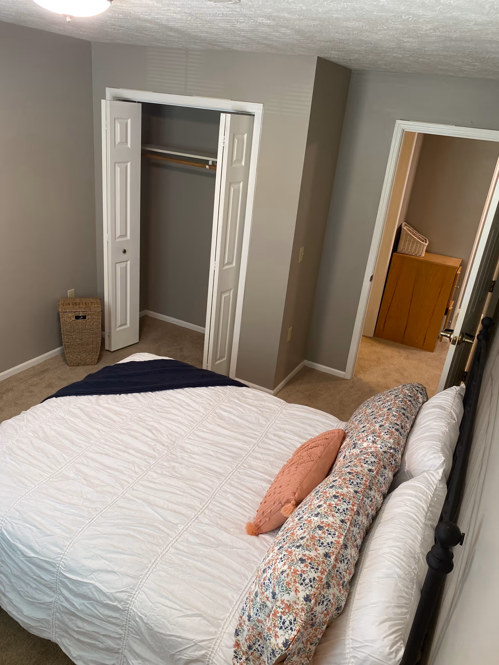 Overhead view of a bedroom with a made bed, open closet, and an adjoining doorway showing a dresser in the hallway.