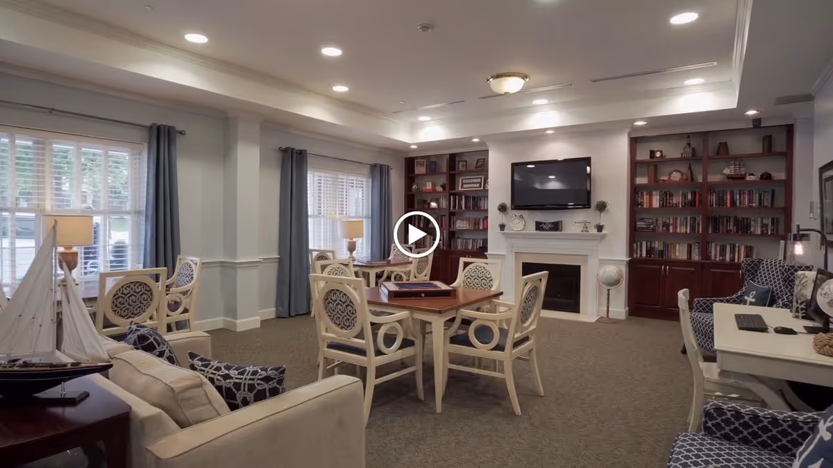 Well-lit communal living room with chairs and tables, a fireplace and TV flanked by bookshelves.