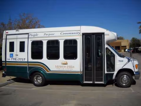 White and green shuttle bus parked outside a senior living facility.
