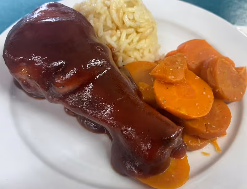 A plate of food featuring a barbecue-glazed chicken drumstick, cooked sliced carrots, and a serving of white rice.